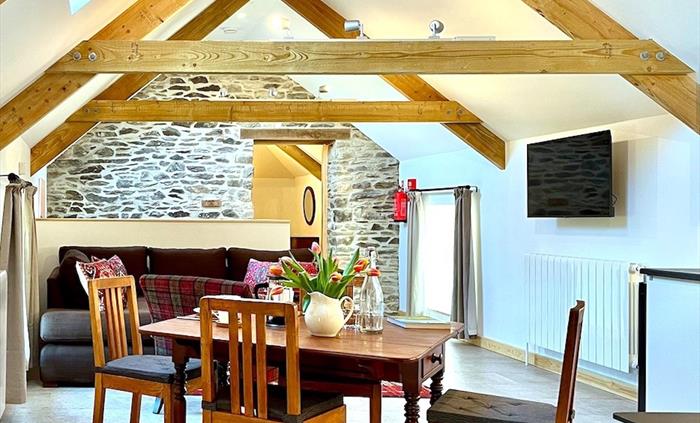 The comfortable lounge area in Y Llofft Stabl has a vaulted ceiling, exposed beams and stonework